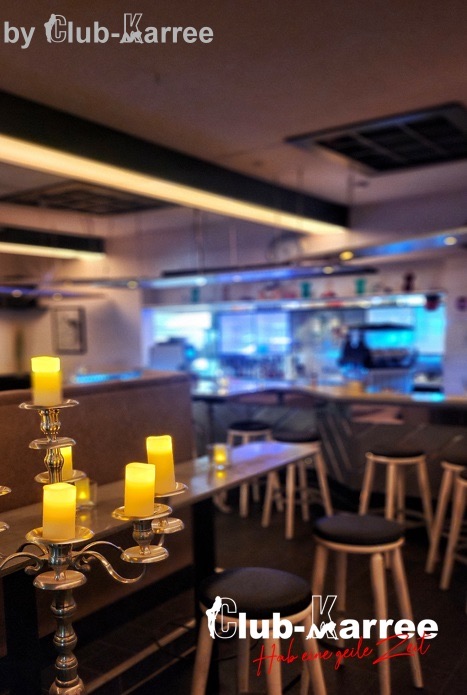 Barbereich mit Kerzenleuchter im Vordergrund und blau beleuchteter Theke.
