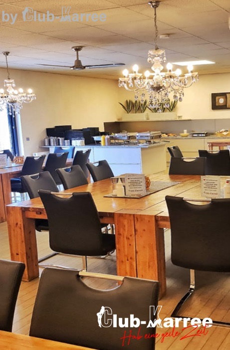 Speisesaal mit Holztischen, schwarzen Stühlen und Buffetausgabe im Hintergrund.