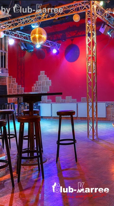 Disco mit roter Wand, Lichttraverse, Spiegelkugel und Barhockern.