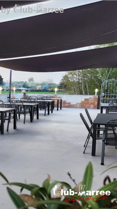 Überdachte Terrasse mit schwarzen Tischen und Stühlen.